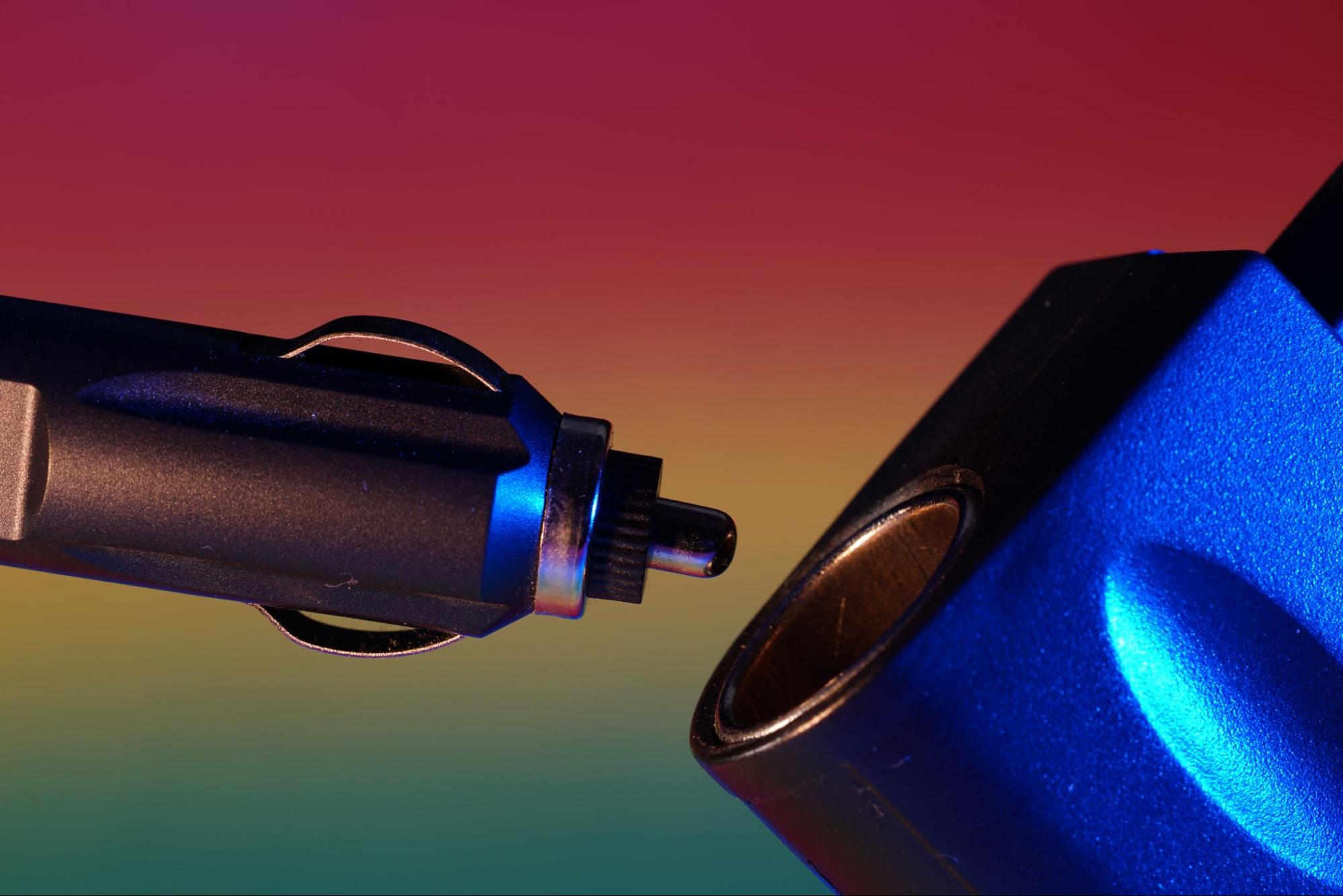 A close-up view of a blue car charger about to connect to a blue vape device, set against a vibrant, multicolored background.