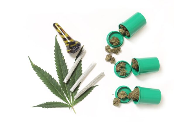 Mairjuana leaf with a glass pipe, joints, and clusters of weed in tubes.