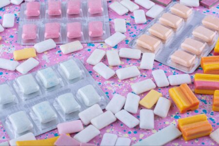 Nicotine gum packs and loose pieces scattered on a vibrant pink background.