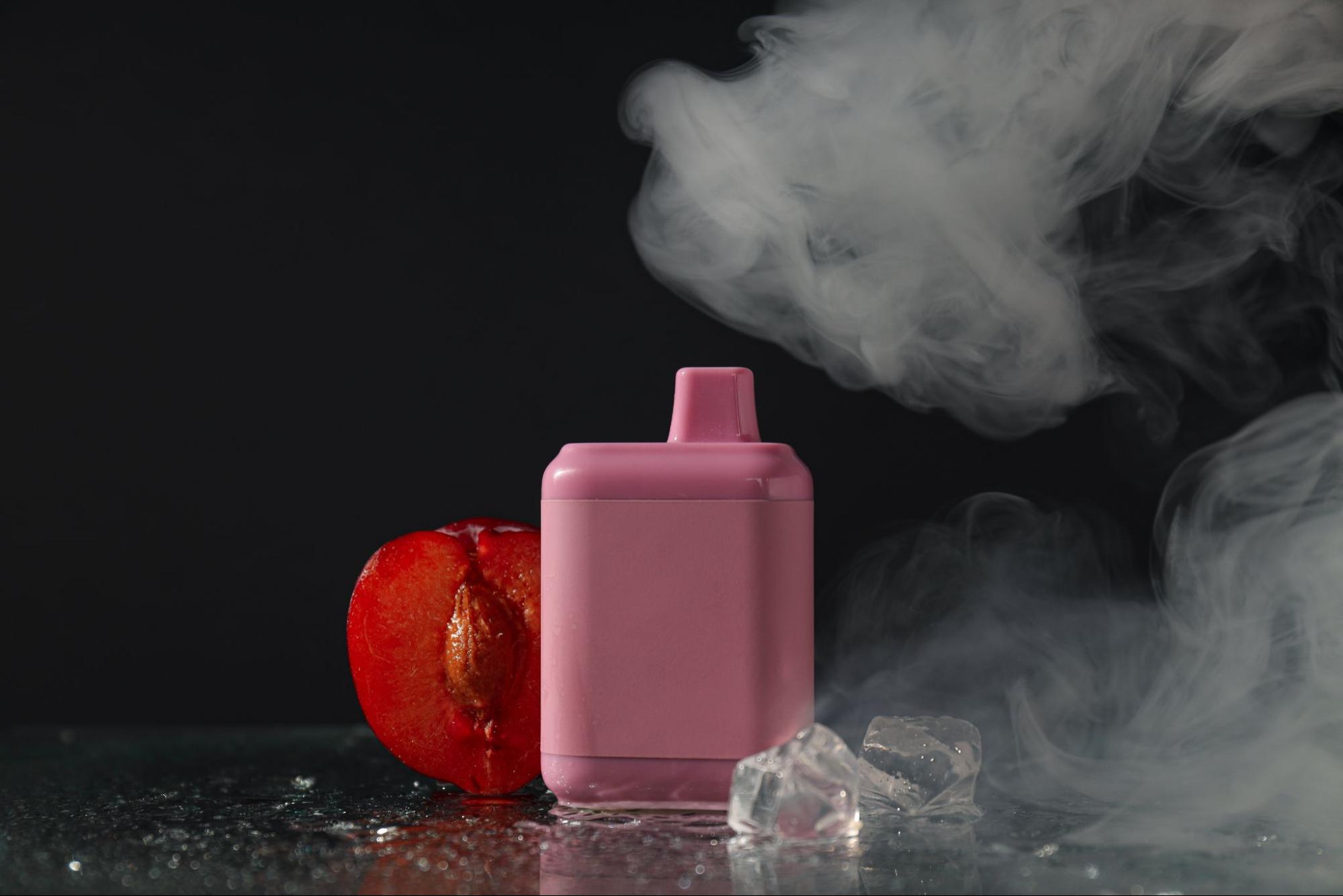 Vaping device next to a fruit cut in half with smoke and ice in the background. 
