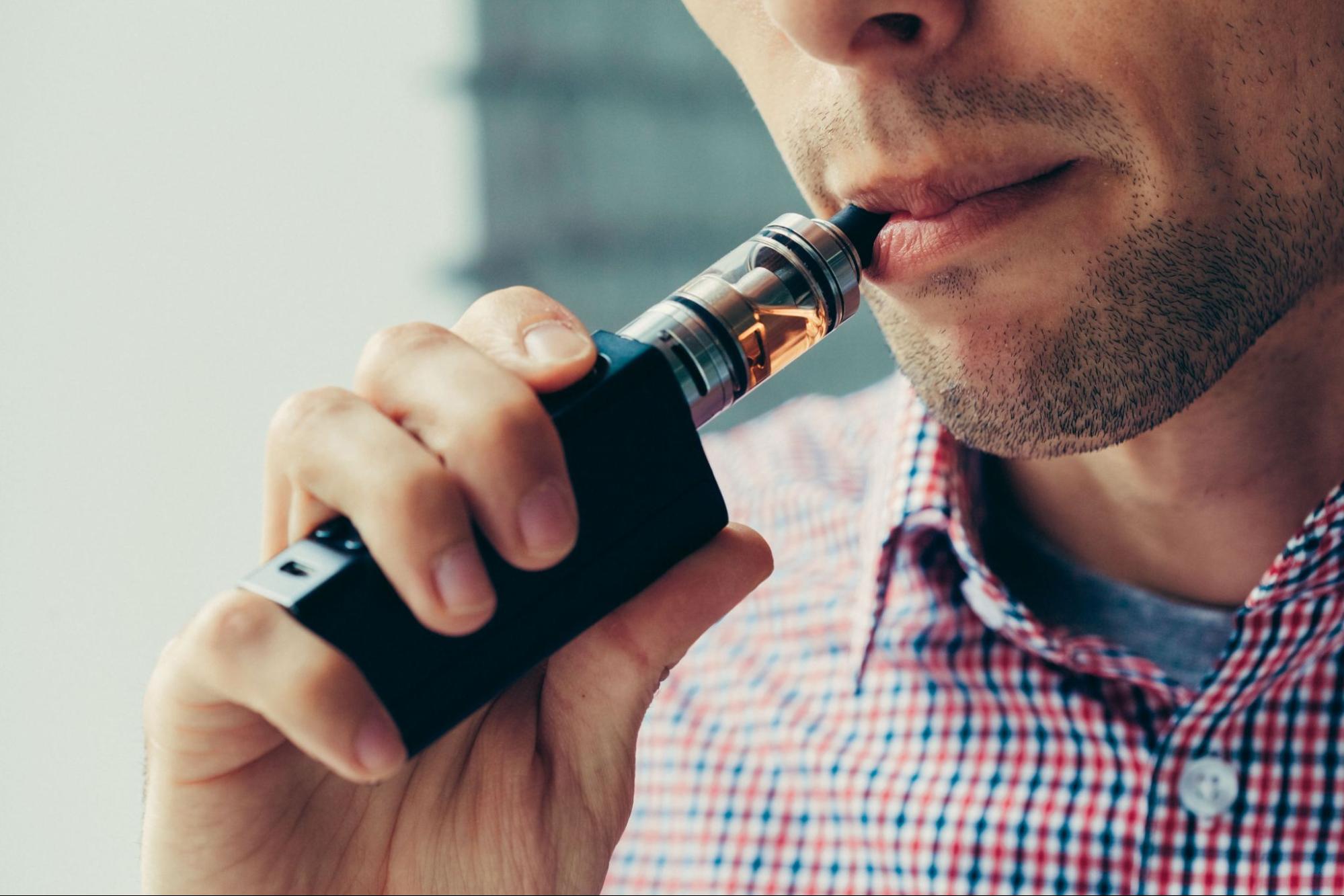 A close-up of a man deeply inhaling vapor from his box mod, capturing the intense moment of vaping satisfaction.