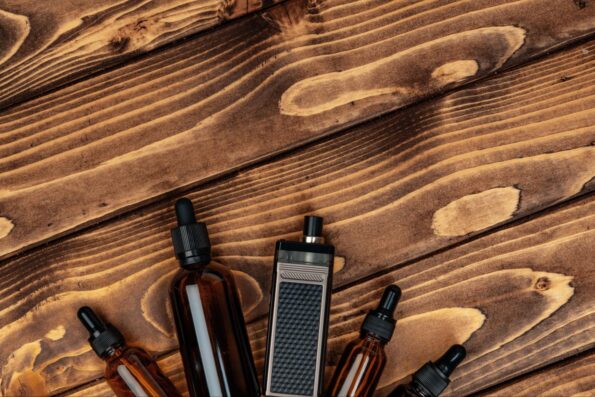 A sleek black vaping device is arranged alongside four different-sized vape juice bottles on a rich brown wooden surface.