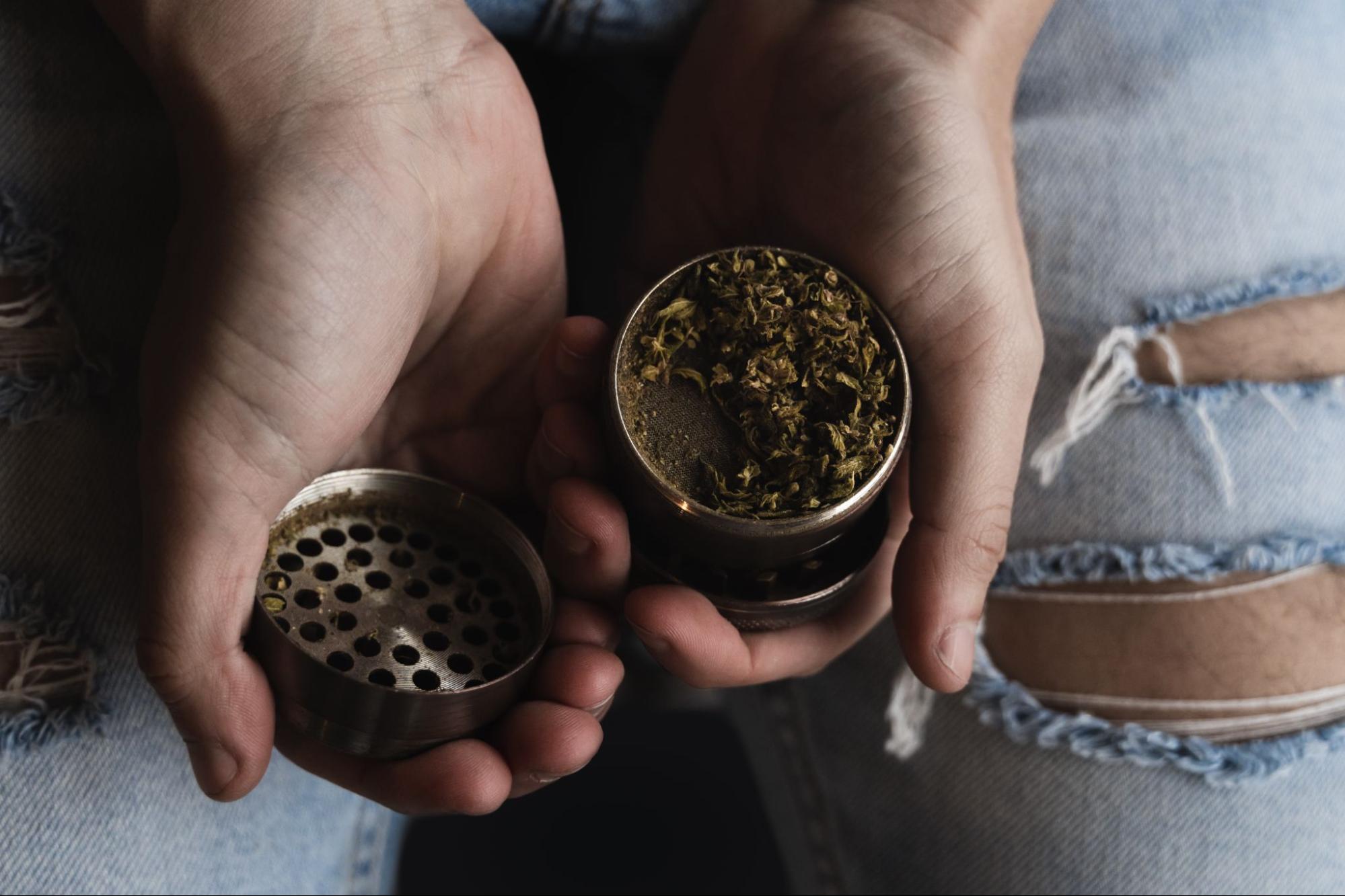 Person wearing jeans and holding a weed grinder. 