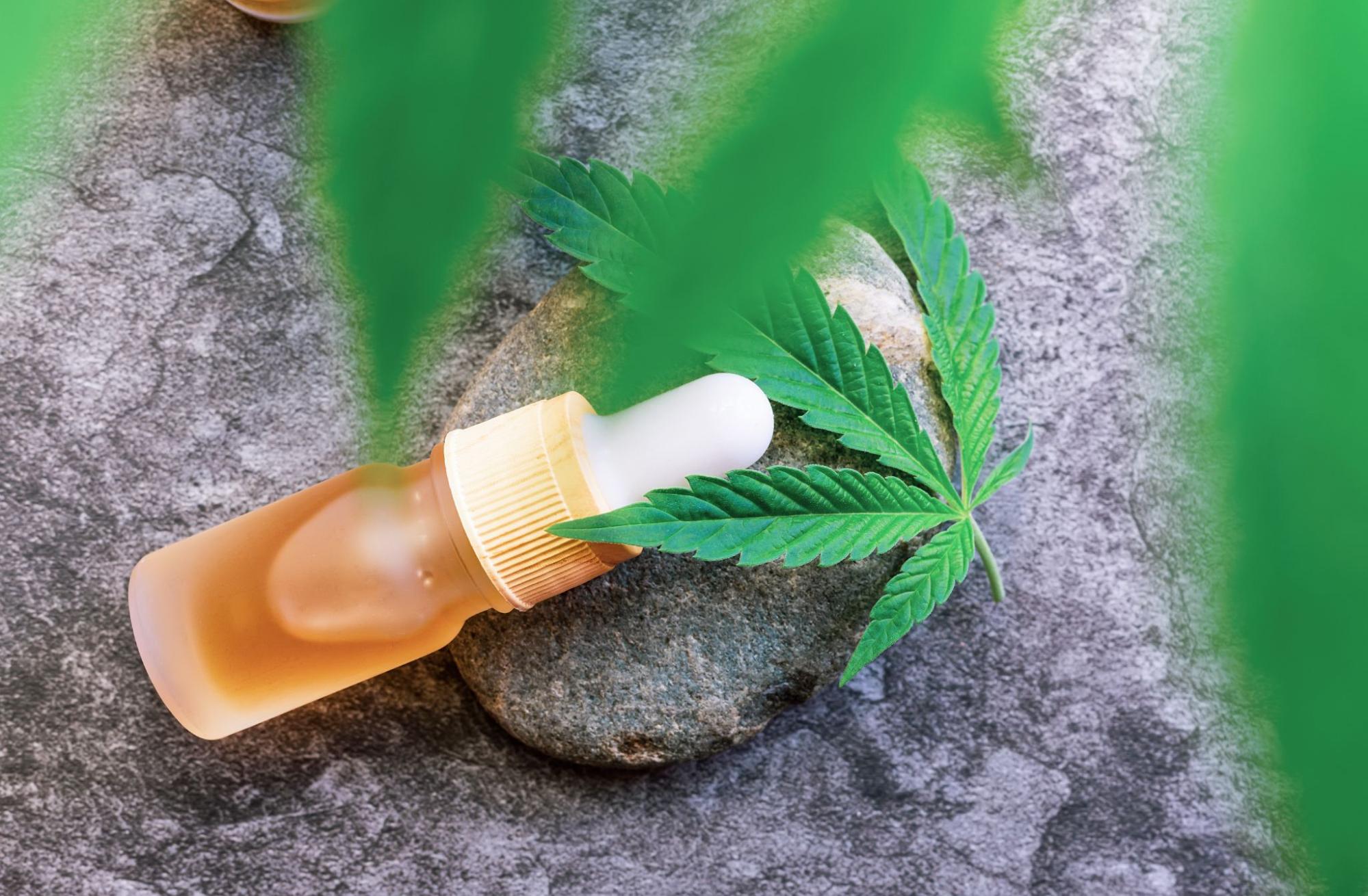 Bottle next to a marijuana leaf on a stone. 