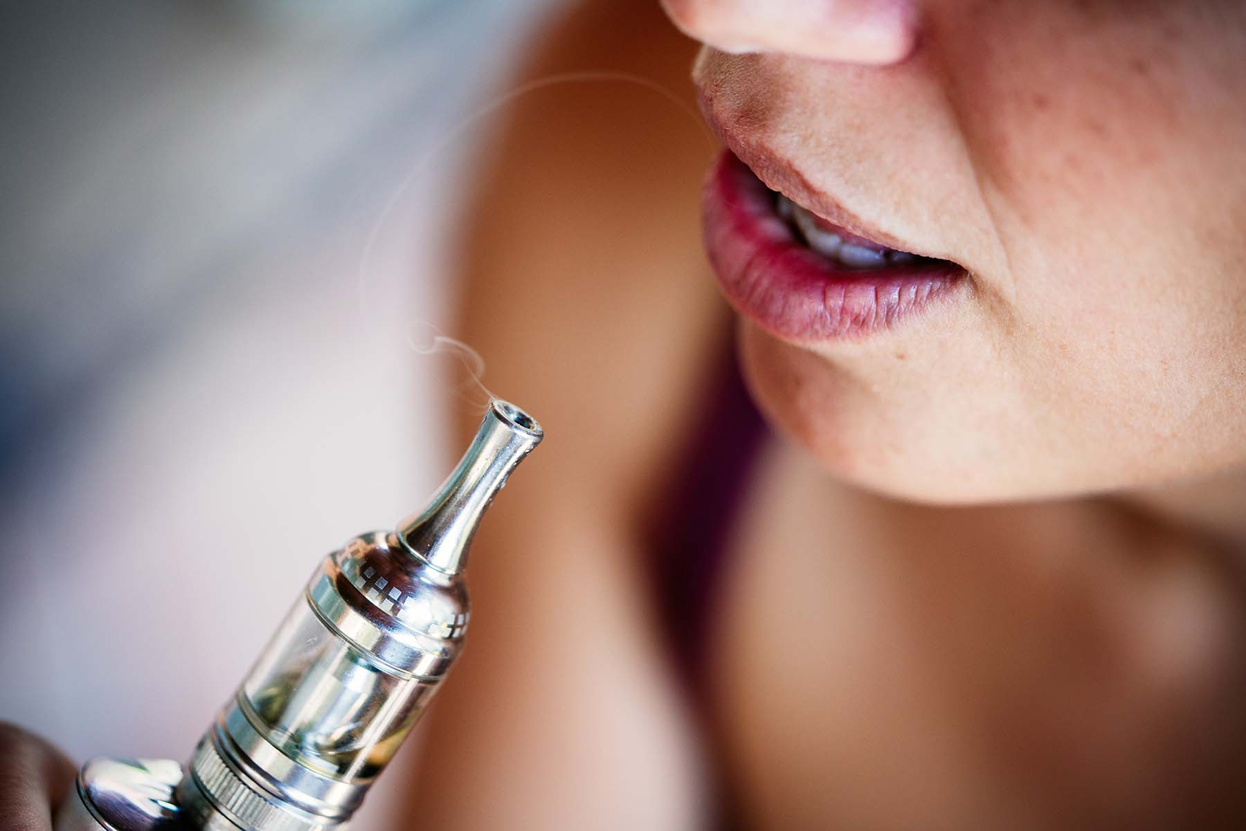 A close-up view of a woman’s mouth exhaling vapor from a vaporizer.