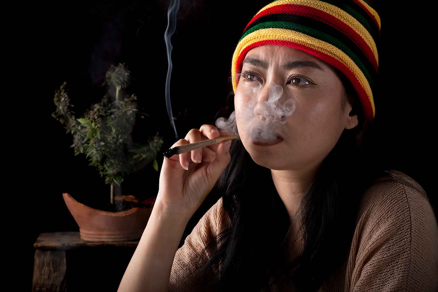 A woman with black hair wearing a Rastafari beanie while smoking a blunt.