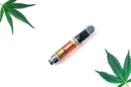 Cannabis vape next to marijuana leaves.