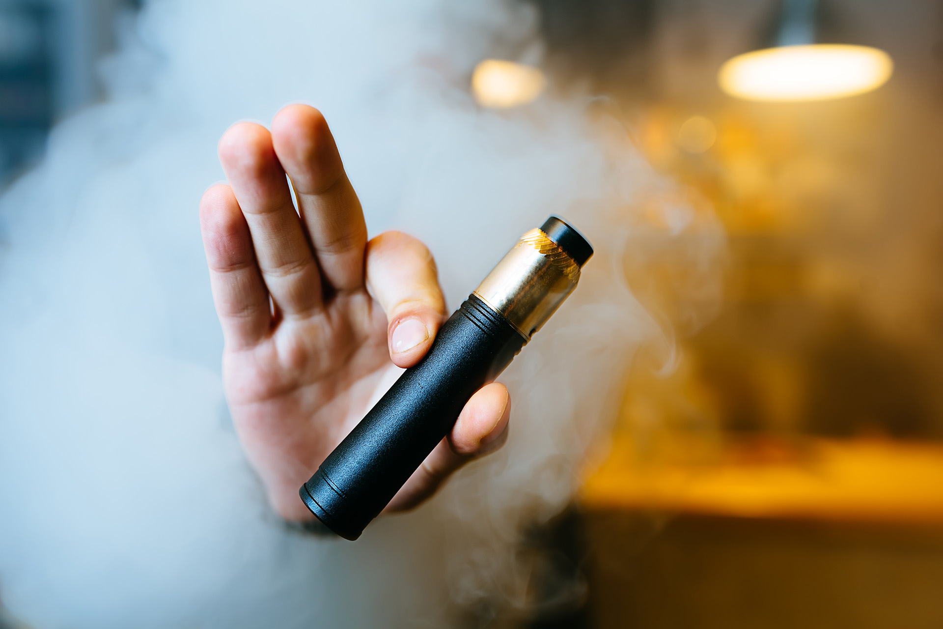 A hand holding a vaping device that’s sticking out of a cloud of smoke.