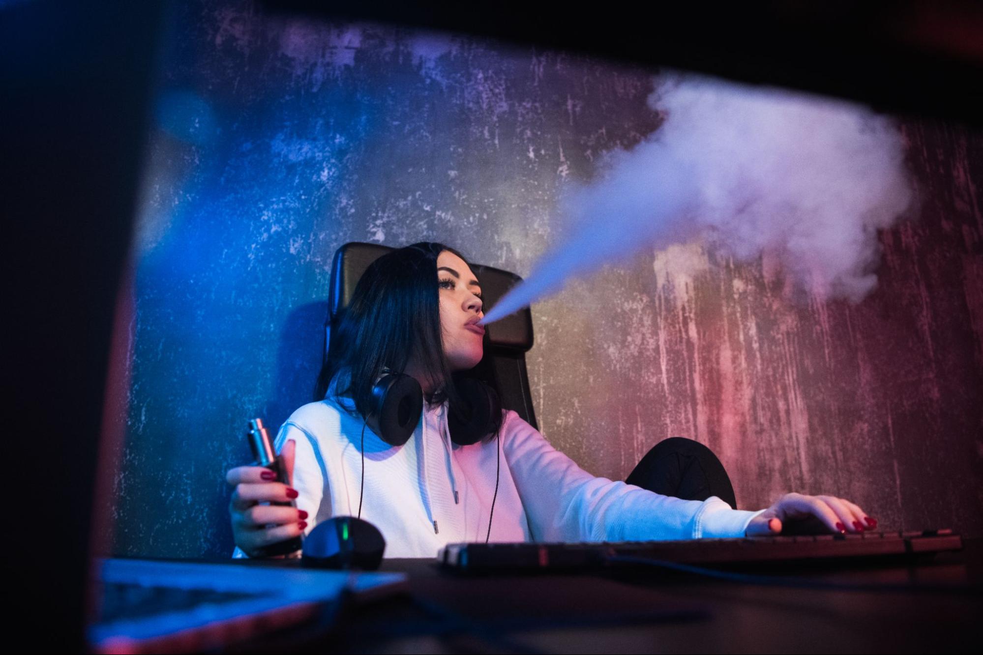 A woman with dark hair blowing clouds from her vape.