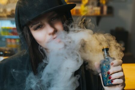 A woman wearing a black hat is vaping.