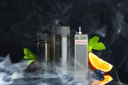 A front view showcases vaping and smoking liquids with fruity flavors against a black background, enveloped by wisps of smoke.