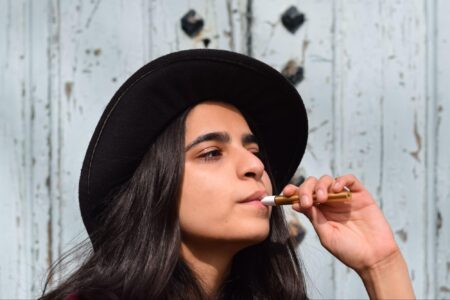 Woman smoking a vape with a white hat on.