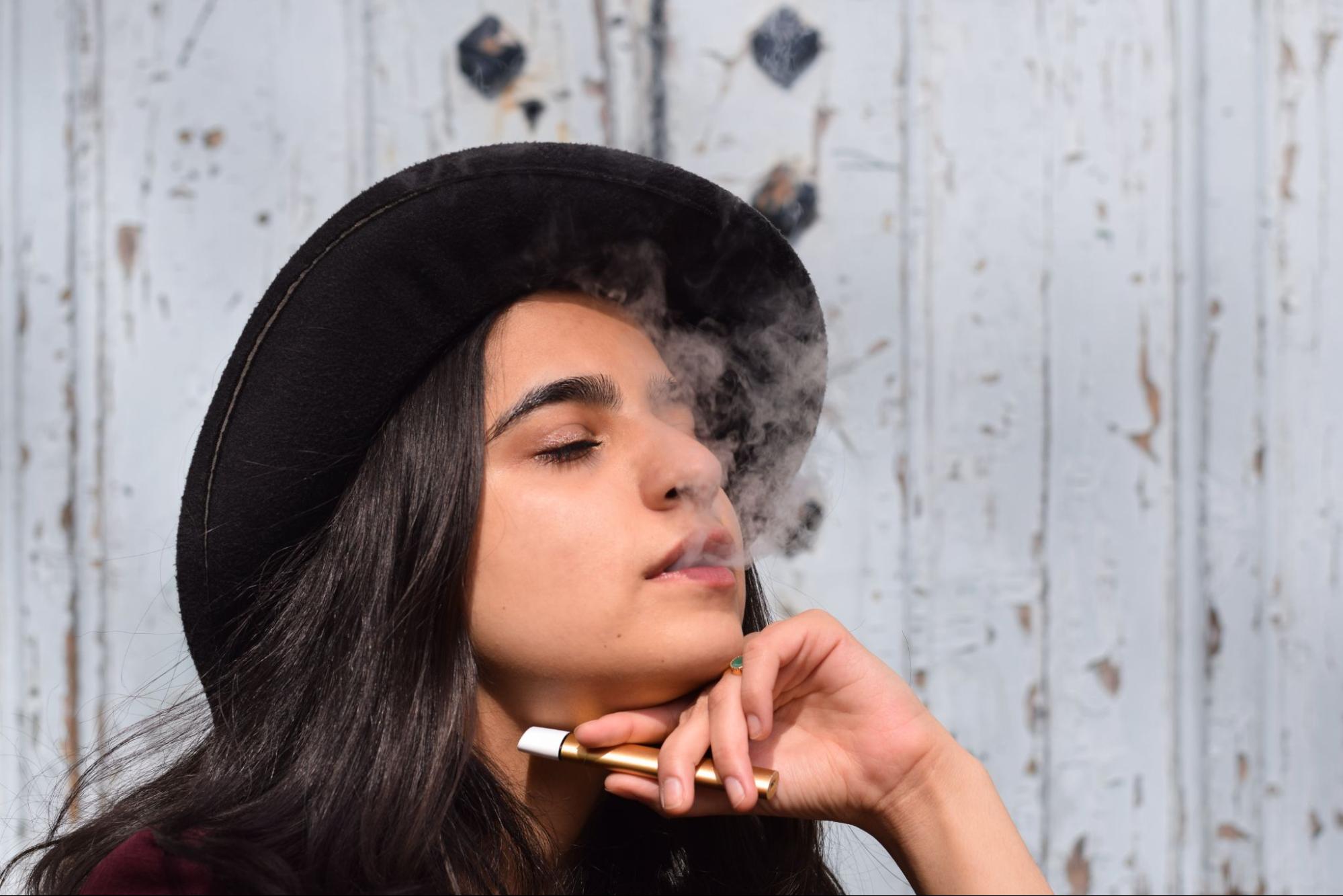 Woman in a hat smoking a vape. 
