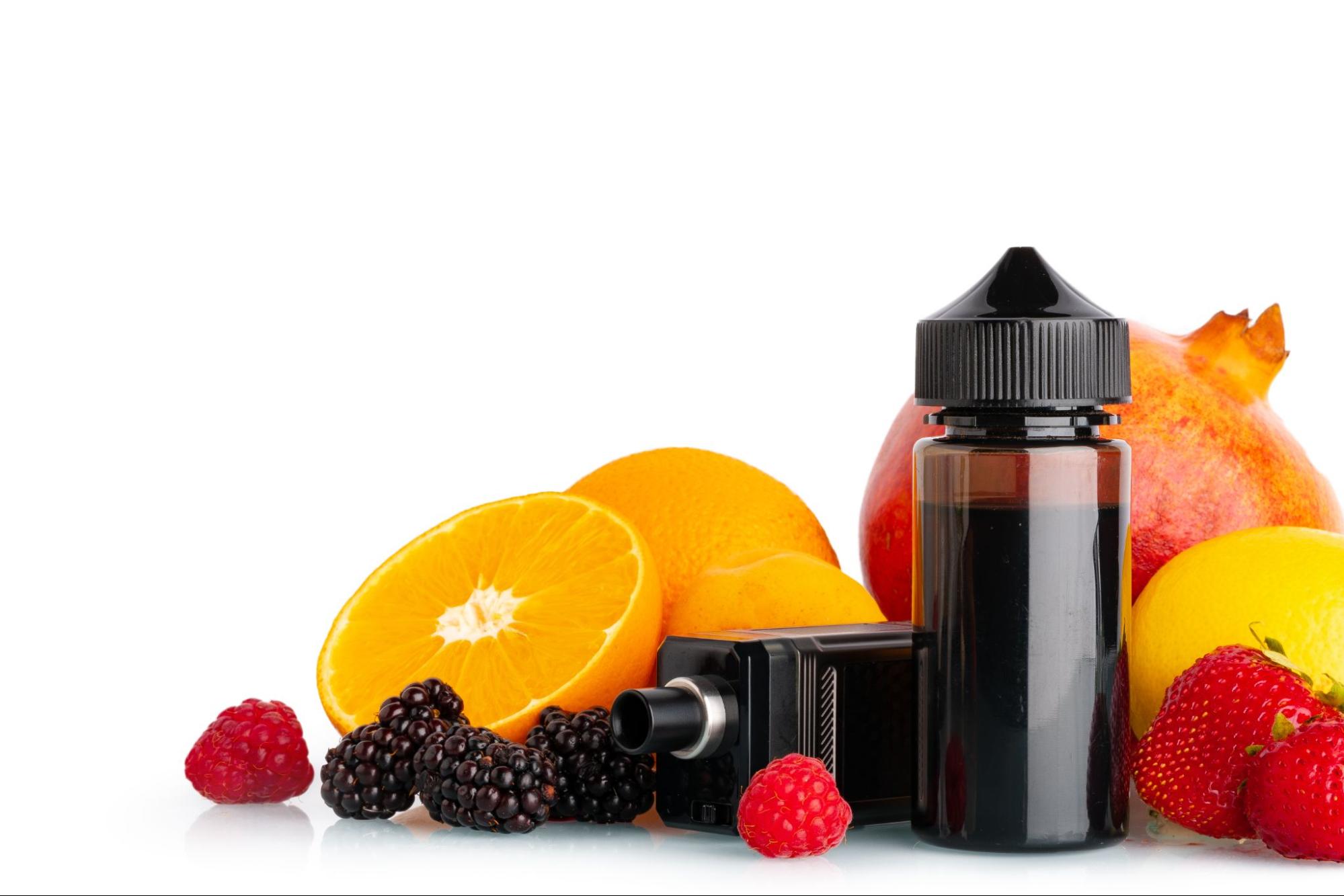 A black vape device lying on its side next to a bottle of e-juice, surrounded by fresh oranges, berries, lemons, and an apple on a clean white background.