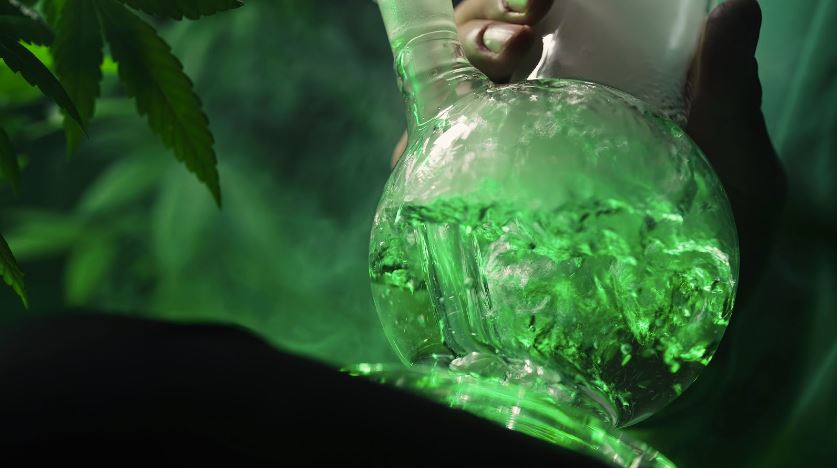 A cropped photo of a man's hand holding a glass bong while inhaling and bubbles forming.