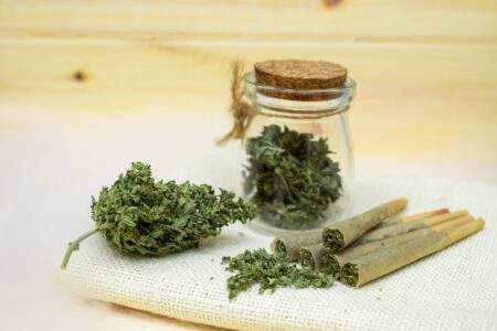 A jar of whole marijuana buds, a large marijuana nug, and rolling cones with marijuana spilling out of them.