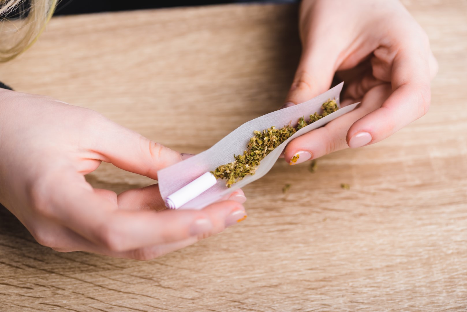 Cropped view of a woman’s hand rolling a joint with a filter over a wood surface.