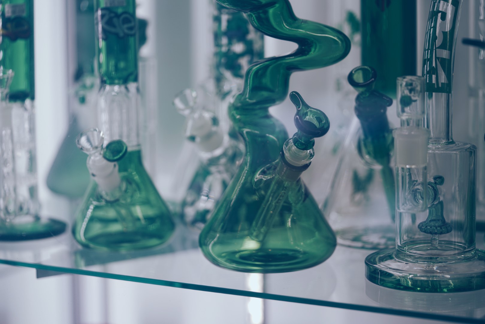 Different types of green and translucent bongs on a glass shelf.