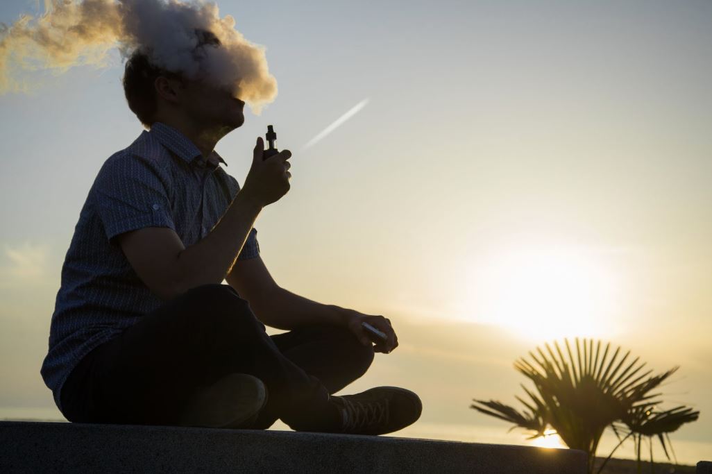 Person vaping with a sunset in the background.