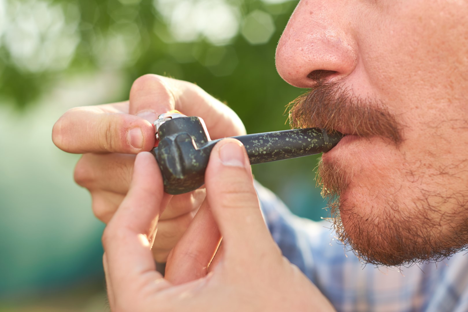 A cropped view of a man holding a lighter up to a spoon pipe while smoking marijuana A cropped view of a man holding a lighter up to a spoon pipe while smoking marijuana