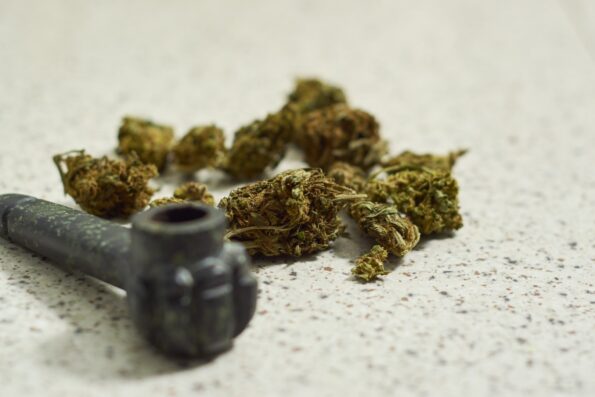 Marijuana buds on a white table next to a spoon pipe.