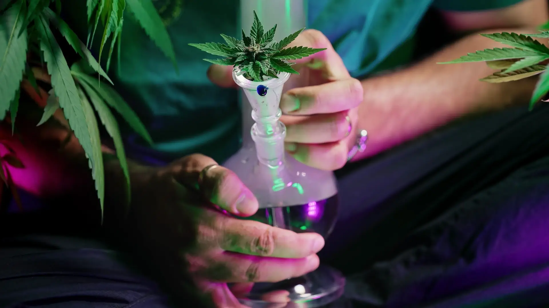 A man holding a glass bong with a marijuana bud sitting inside the bowl.