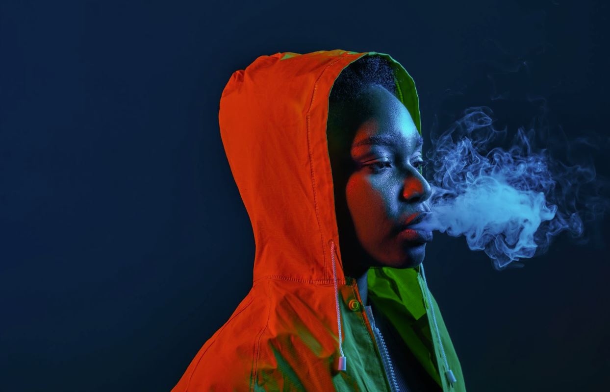 A person with a hooded jacket exhaling smoke.
