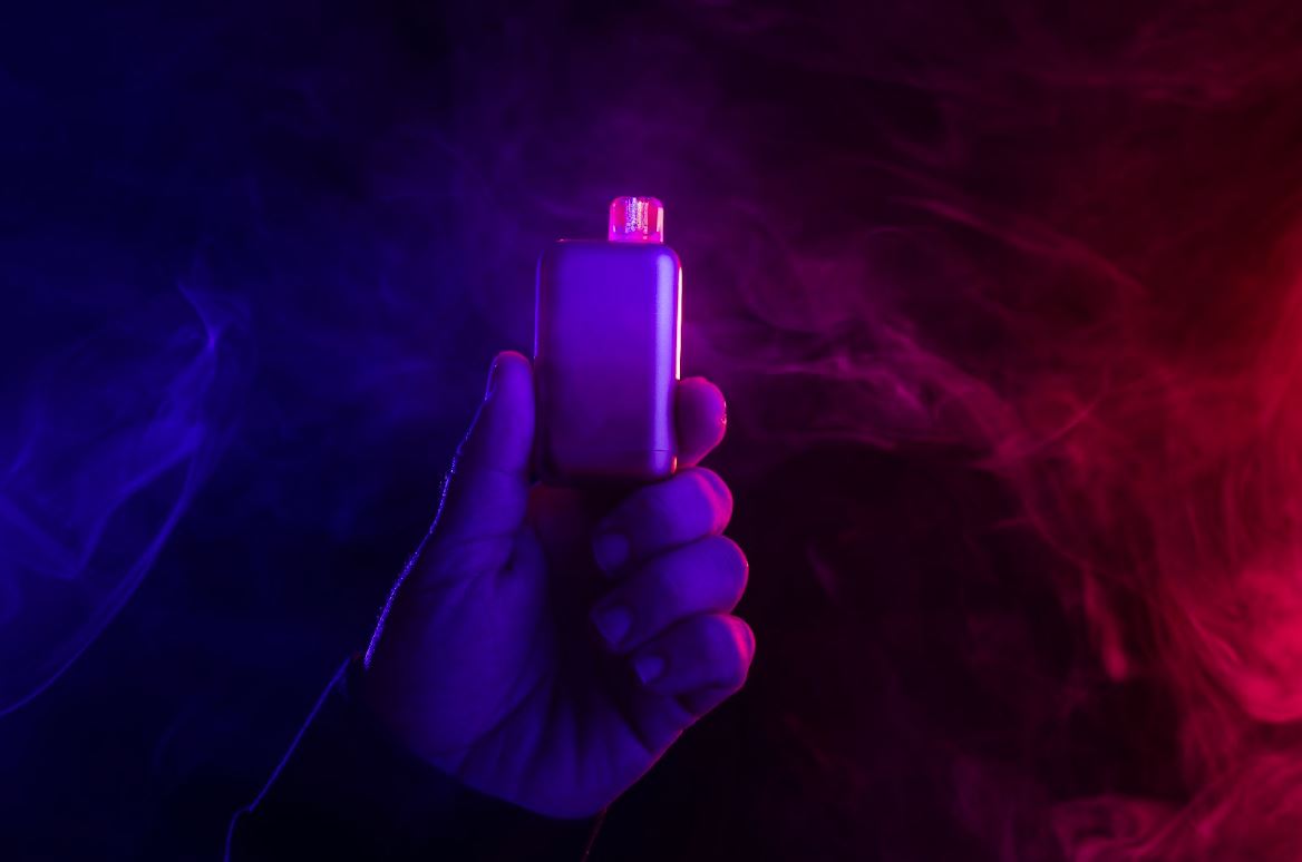 A person holding a vape device with smoke in the background.