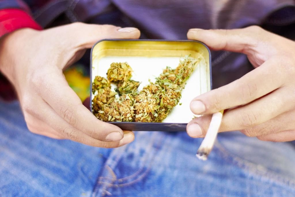 Man with a tin of marijuana and a joint.