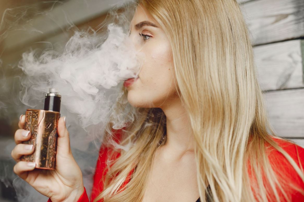 Woman exhaling smoke with a vape device in her hand.