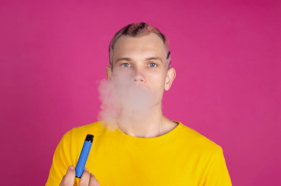 Man exhaling smoke and holding a vape.