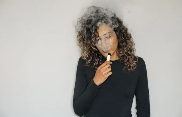 Woman exhaling smoke while holding a vape.