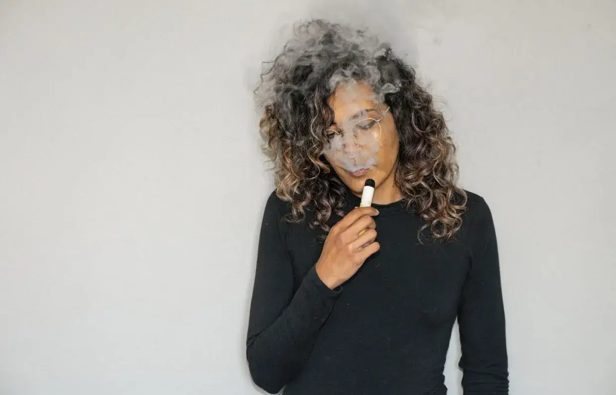 Woman exhaling smoke while holding a vape.