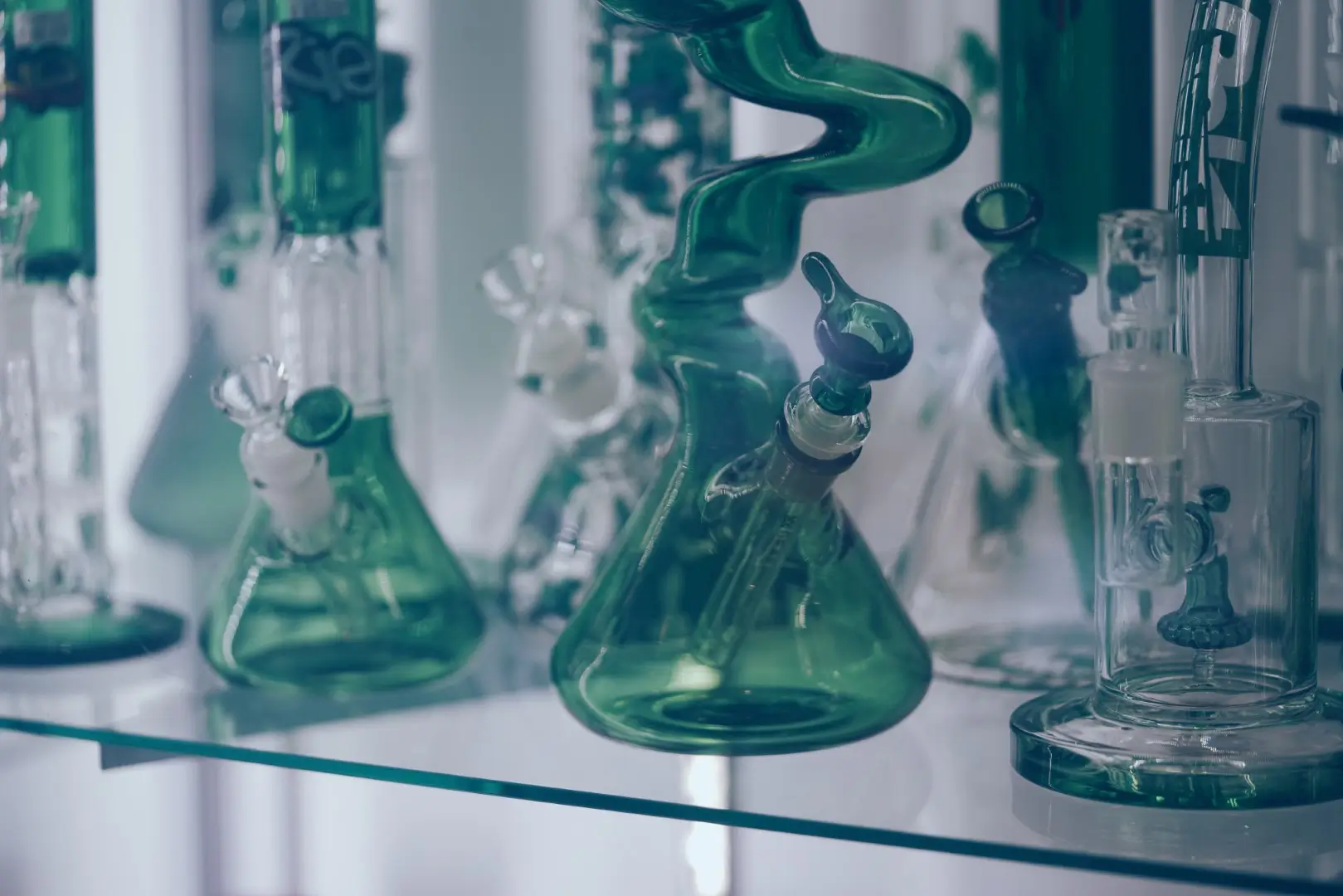 Multiple green and clear glass bongs sitting on a table.