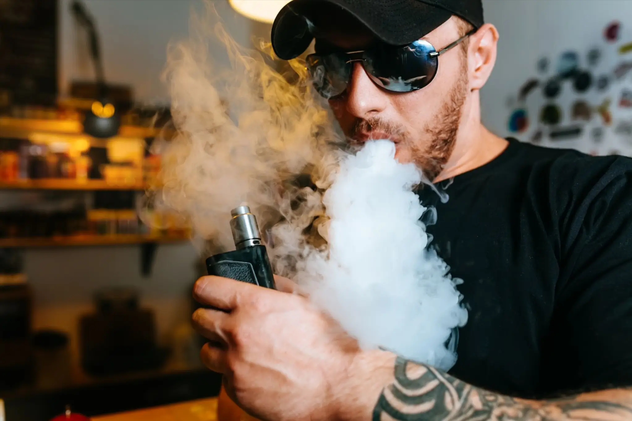 A man holding a vape device and blowing a large cloud of vapor.