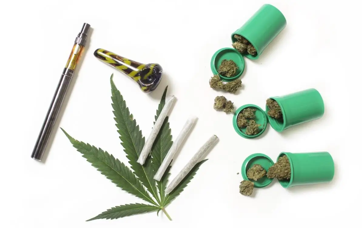 A marijuana leaf, wax pen vaporizer, glass pipe, joints, and open bottles with weed spilling out against a white background. A concept for the best way to smoke weed.