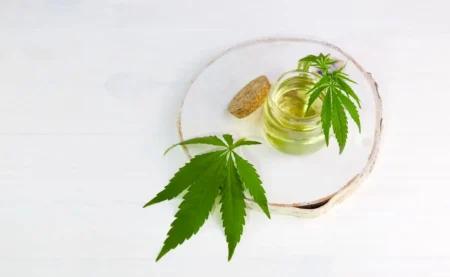Cannabis concentrate in a jar surrounded by two cannabis leaves against a white background.